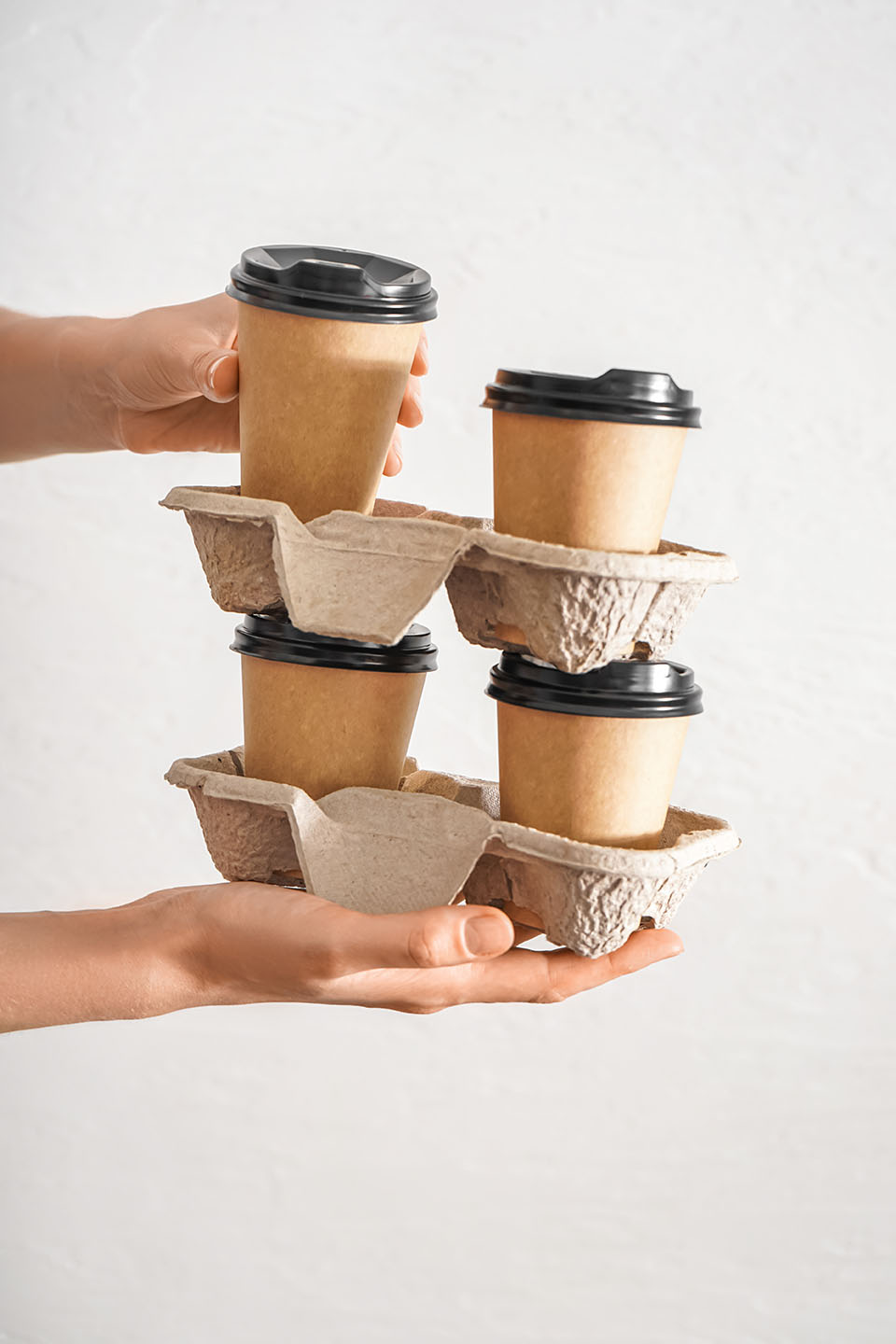 Woman holding holders with paper cups of coffee on light background